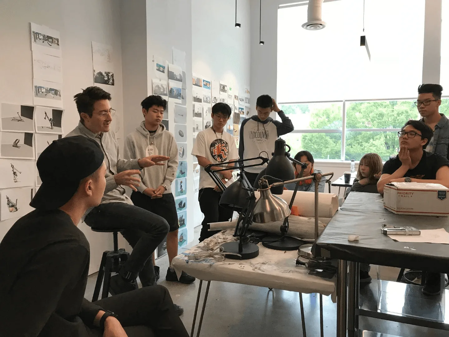 Instructor leading a group critique with teen students in a studio lined with pinned-up sketches